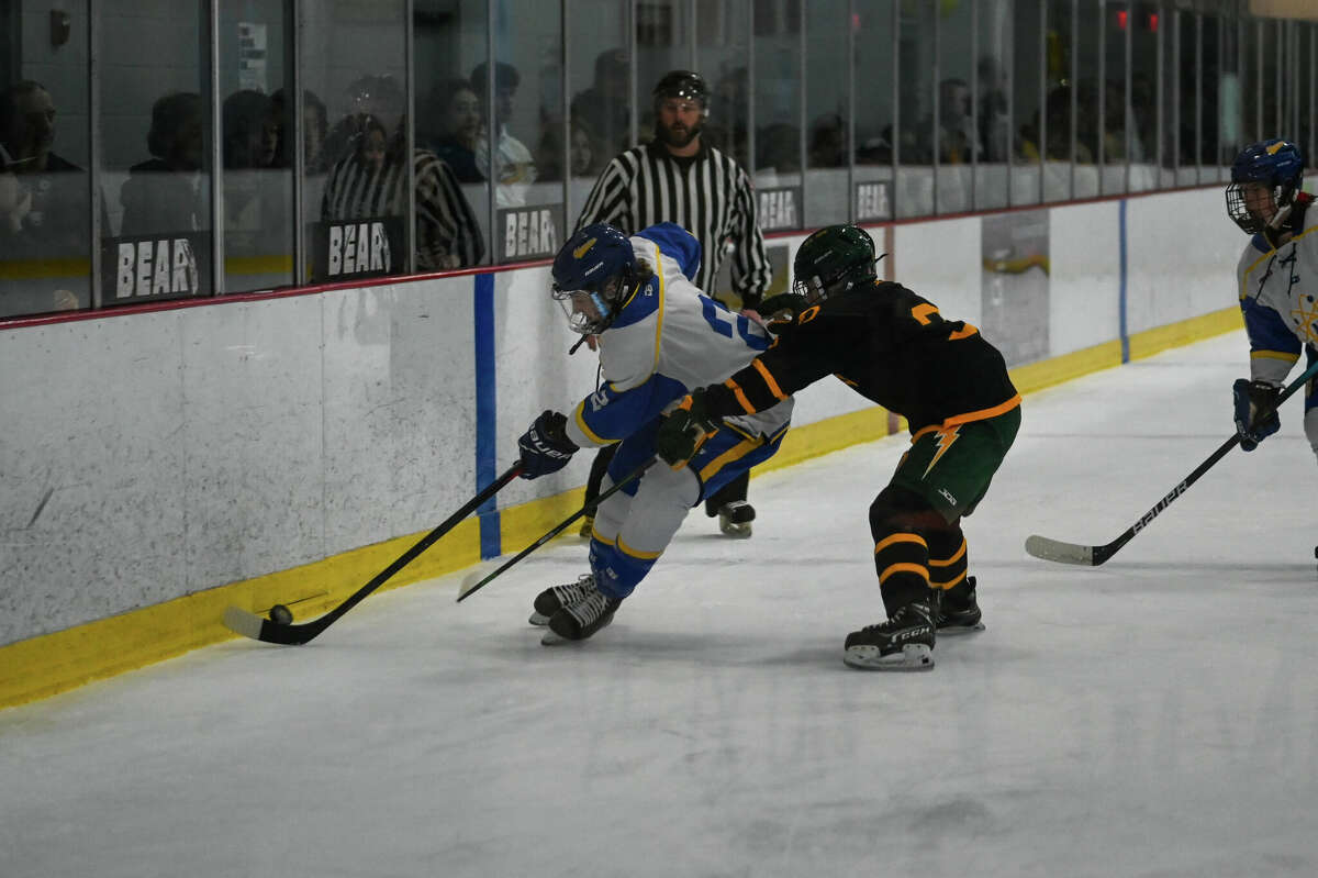 Midland High's Cade Sanborn digs the puck out along the boards during Wednesday's game against Dow High, Dec. 7, 2022.