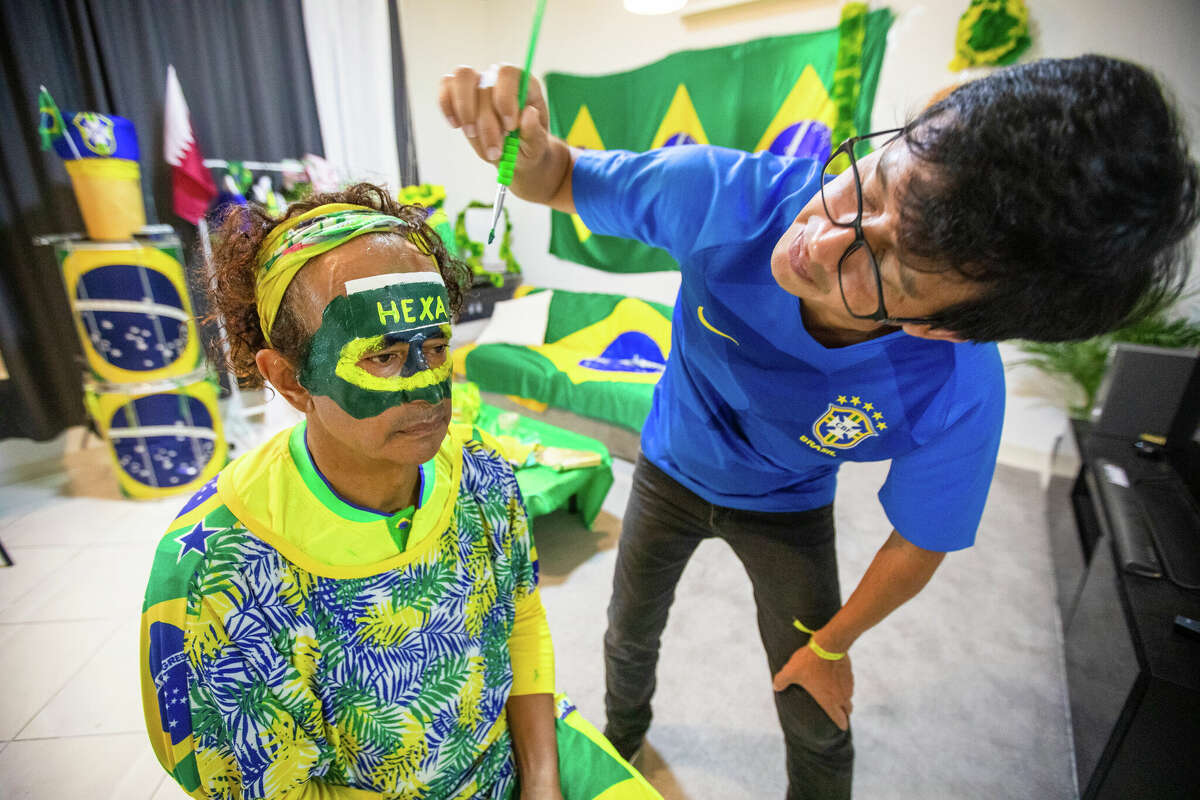 Brazilian Wallace Leite has his face painted by roommate Lucivaldo Costa before the Brazil and Switzerland World Cup game in Doha, Qatar on November 28, 2022.