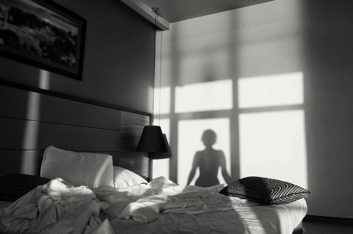 Young woman is sitting on the bed, shadow on the wall. Silhouette of a girl in front of a window black and white art photography monochrome, photo noir, retro.