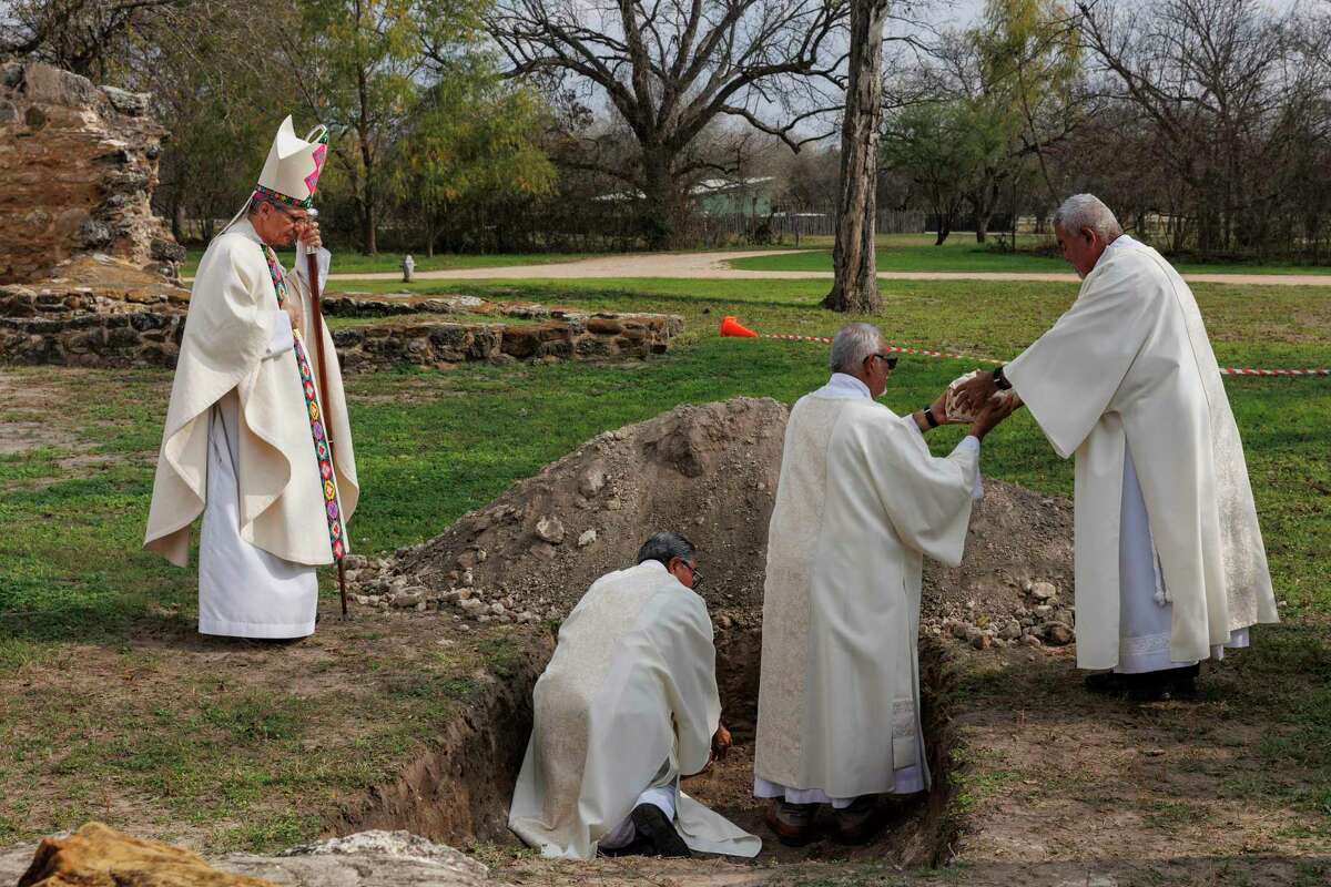 San Antonio Archbishop Gustavo García-Siller, left, watches as members of the catholic clergy gently place ancestral human remains in a freshly dug grave at Mission San Juan on Friday.