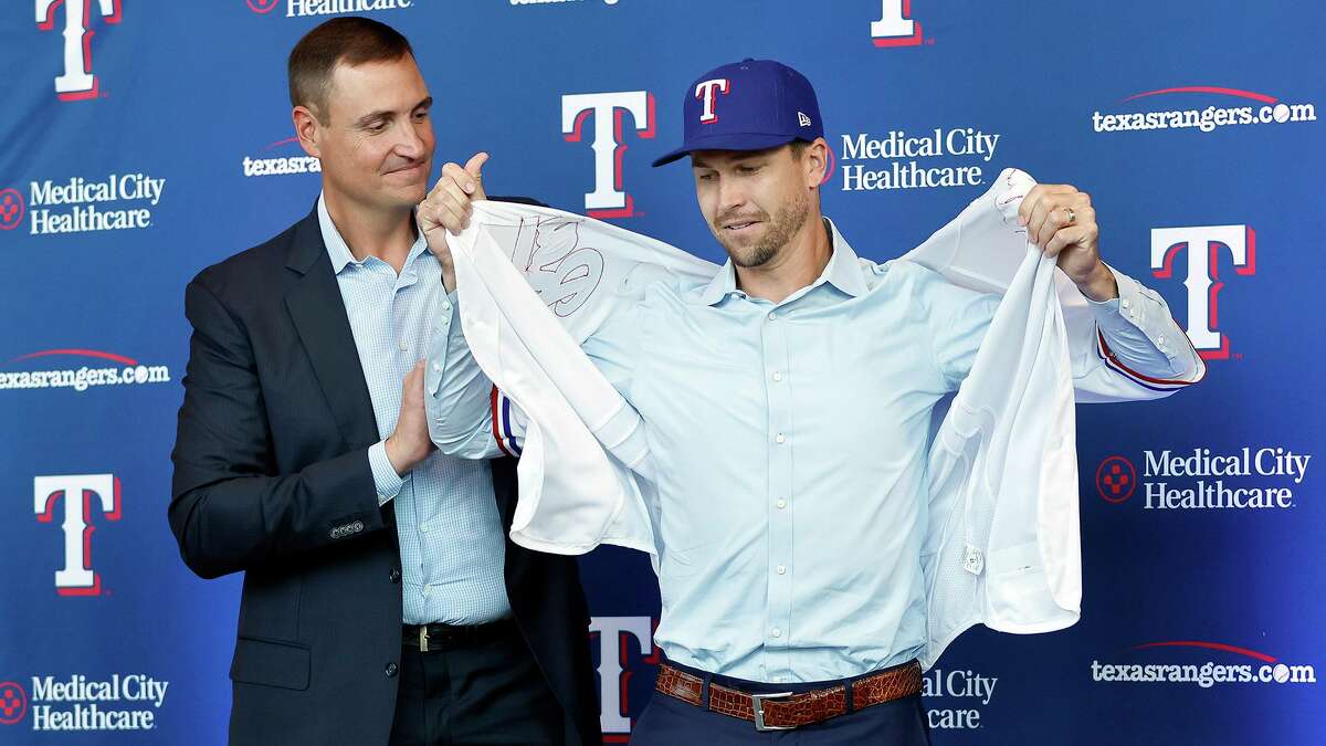New Texas Rangers starting pitcher Jacob deGrom tries on his new jersey with the assistance of General Manager Chris Young during his introductory press conference at Globe Life Field in Arlington, Dec. 8, 2022. deGrom signed a five-year contract until the year 2027.