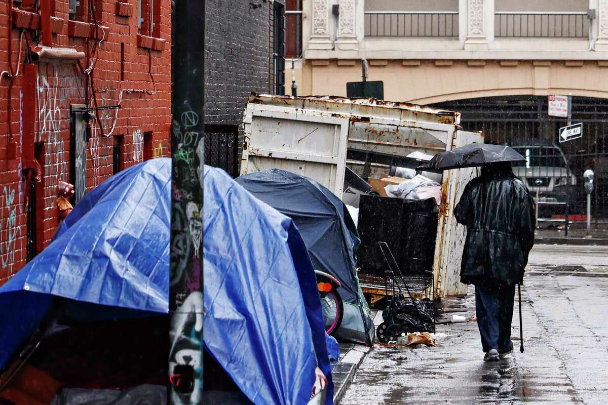 一份新报告称，加州每年只需花费81亿美元就能解决无家可归问题。2022年12月1日，在加利福尼亚州旧金山的默特尔街，一名男子打着伞，走过一排覆盖着防水布和雨伞的帐篷。