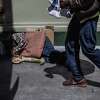 A pedestrian passes a person sleeping on a street in the Tenderloin in San Francisco, Calif., on Tuesday, Aug. 23, 2022. California Governor Gavin Newsom vetos supervised drug consumption sites in SF and LA.