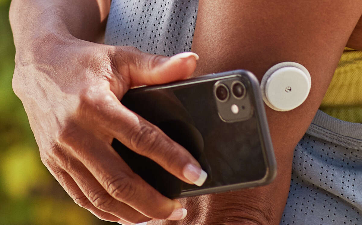A user holds a smartphone over the FreeStyle Libre 2 sensor to check glucose levels. The technology is the same used with Apple Pay or Google Pay. 