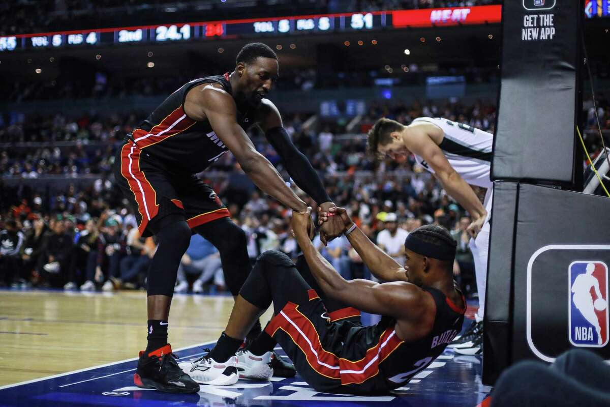 The Heat’s Bam Adebayo helps teammate Jimmy Butler to his feet during Saturday’s game against the Spurs at Arena Ciudad de Mexico in Mexico City.