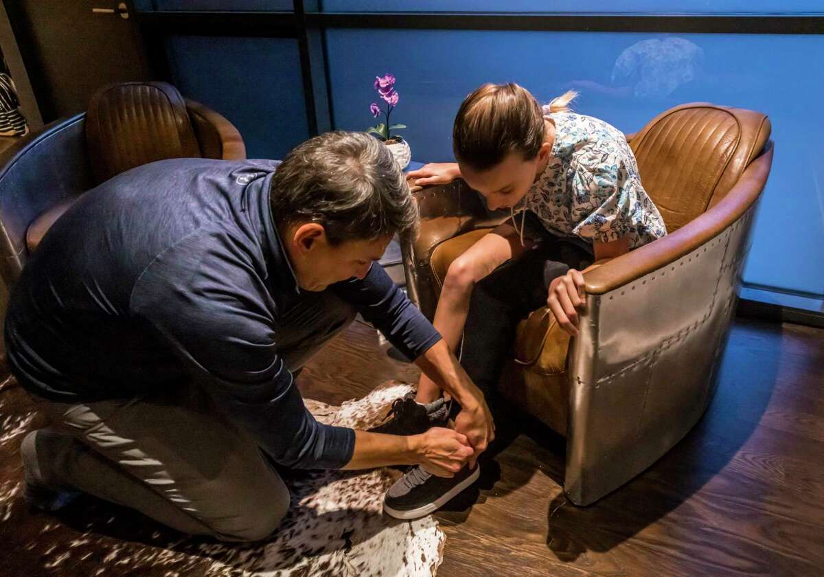 Jeremiah Robison helps his 13-year-old daughter Sophia put on her shoes for a quick walk at their home in San Francisco.  Sophia wears a wristband her father, the founder and CEO of Cionic, invented to help people with mobility problems.