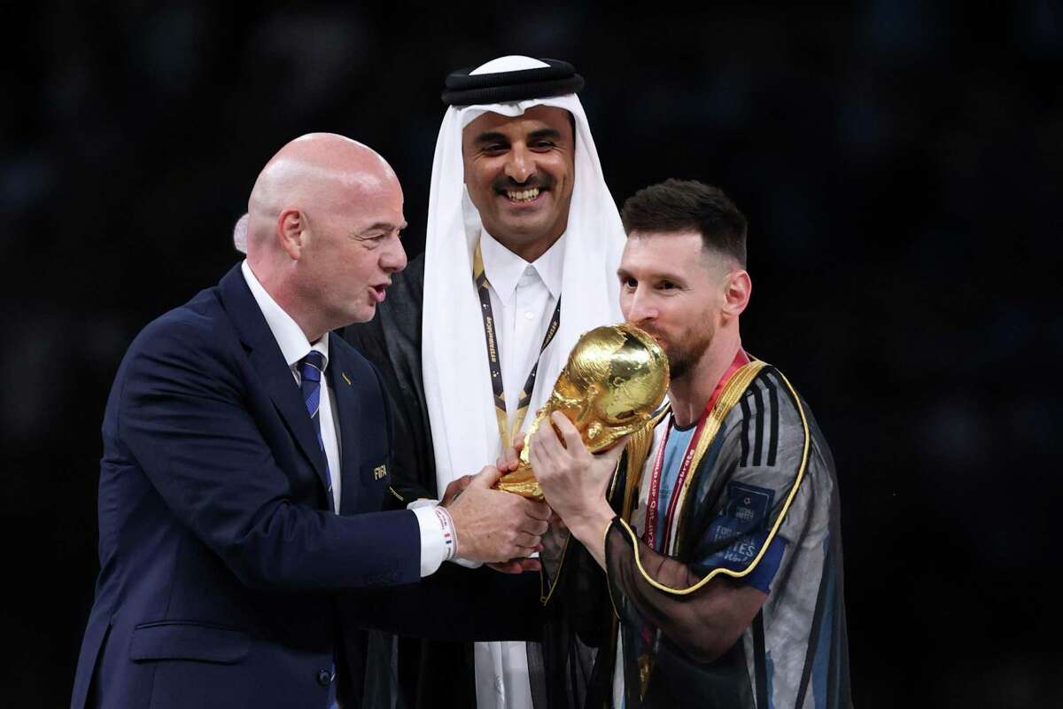 Lionel Messi wears a traditional Qatari robe over his uniform next to FIFA boss Gianni Infantino and Sheikh Tamim bin Hamad Al Thani, Emir of Qatar.