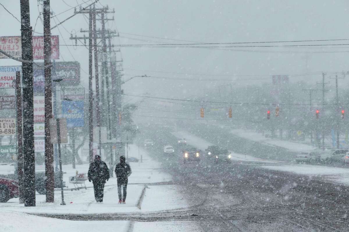 People walk along Blanco Road as a brisk snow falls on Thursday morning, Feb. 18, 2021.