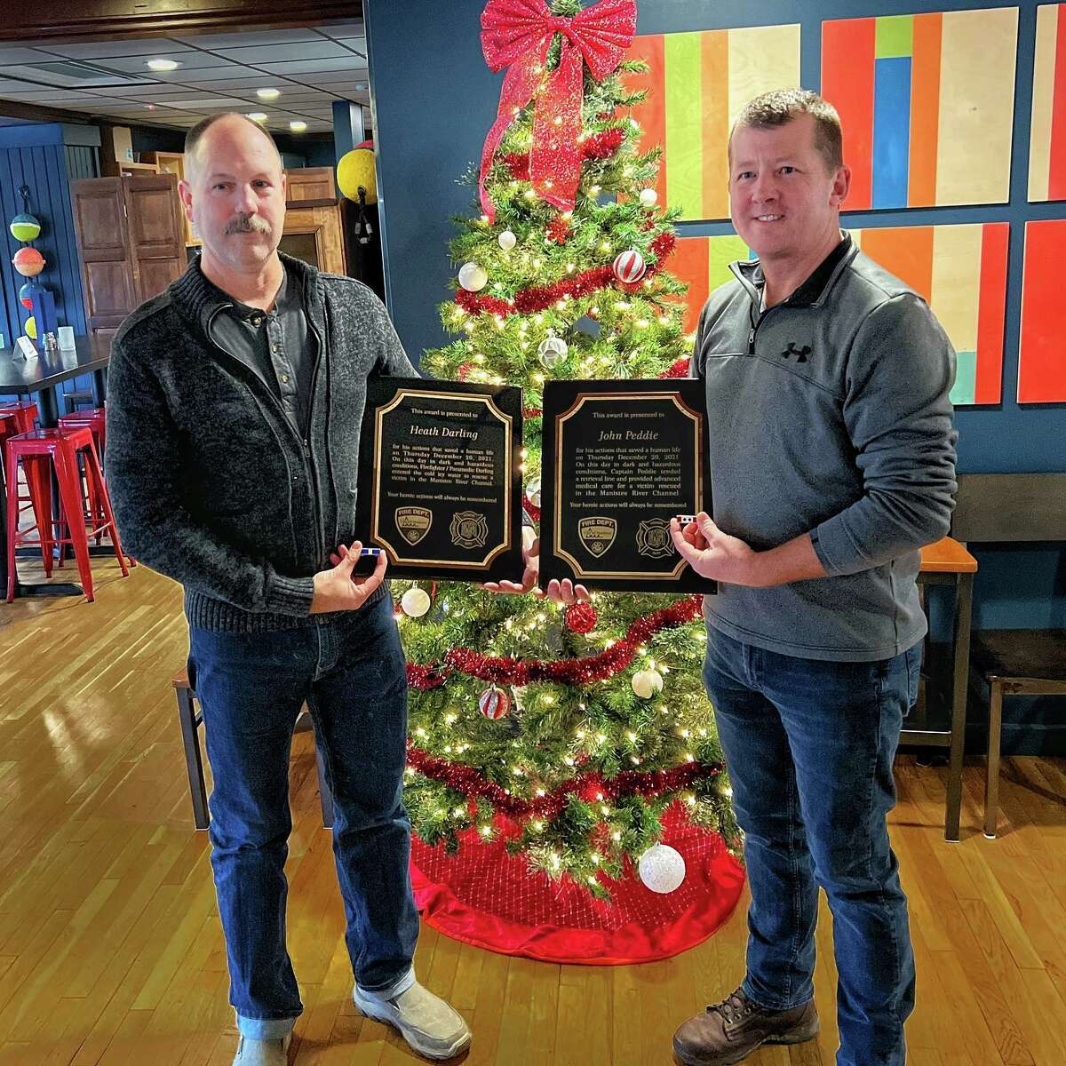 (From left) Firefighter medic Heath Darling and Captain John Peddie, of the Manistee City Fire Department, received placards recognizing their efforts in rescuing a man from the Manistee River Channel in January.  