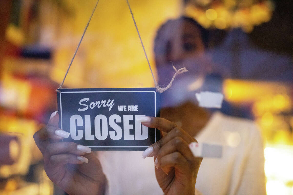 Woman putting closed sign on glass front door of coffee shop