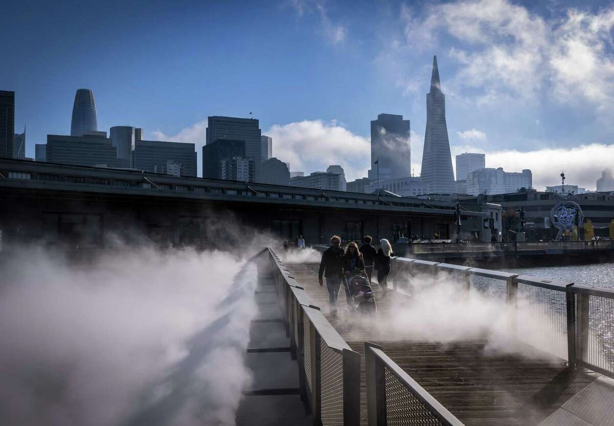 Samuel Riezzo and Susan Bloom walk their daughter Willa over the fog bridge at the Exploratorium as fog rolls in around the Transamerica Pyramid in San Francisco, Calif., on Sunday, October 30, 2022. The city’s iconic Transamerica Pyramid turns 50 years old later this year and remains one of San Francisco’s more cherished and well-known buildings.