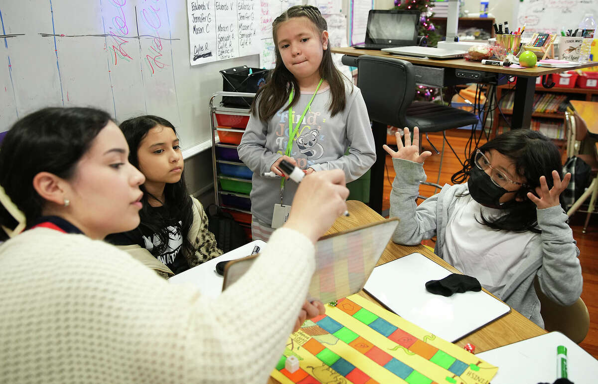 Angelina Castillo demonstrates how she works with Briscoe Elementary School third graders Kaylee Mendoza, from left, Cylie Ramos, and Valery Lopez on their math skills on Tuesday, Dec. 20, 2022 in Houston.