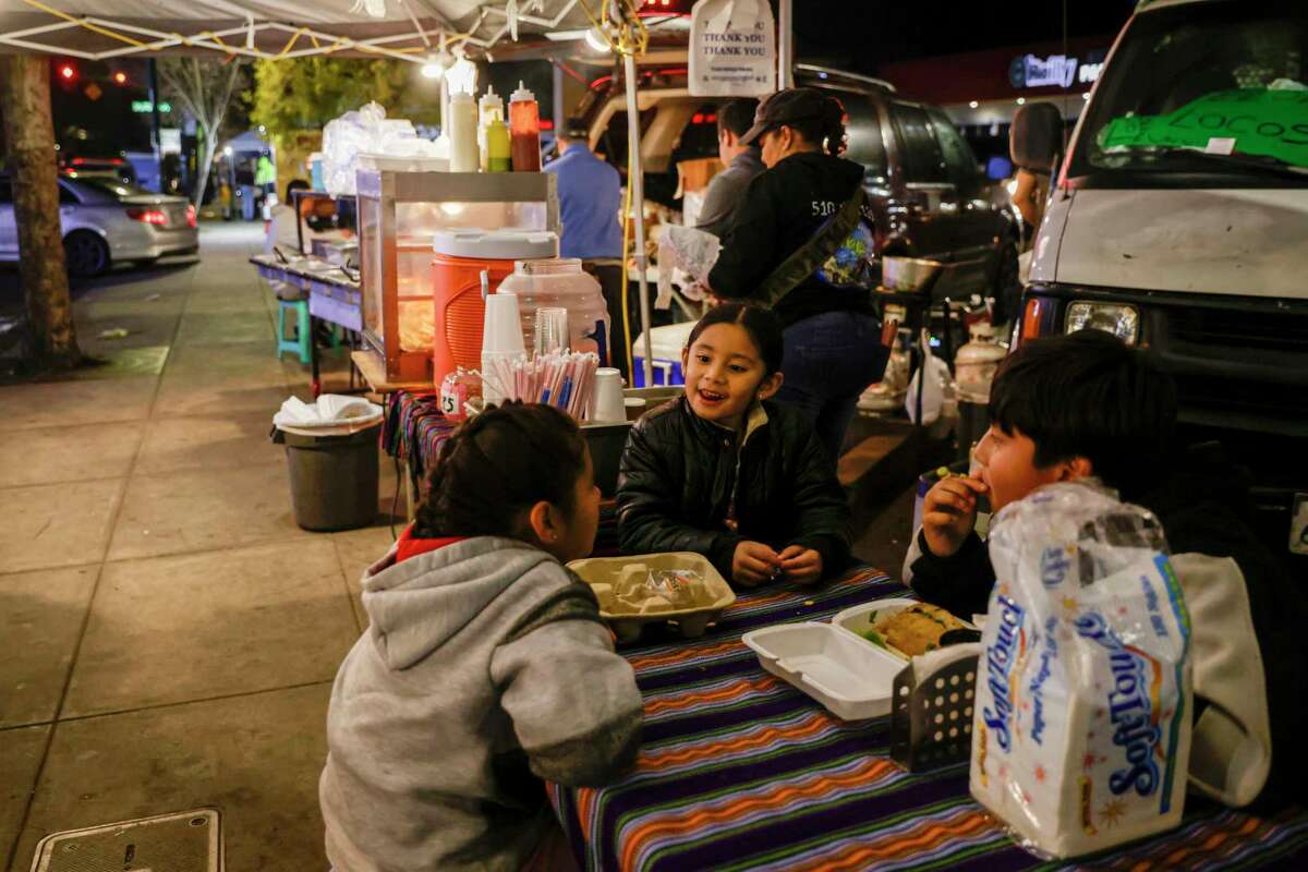 From left, Leidy Solorsano, 7, Mia Rodriguez, 6, and Jonathan Rodas, 11, enjoy tacos while their family serves Guatemalan food in Fruitvale in Oakland, Calif. on Wednesday, Dec. 21, 2022.