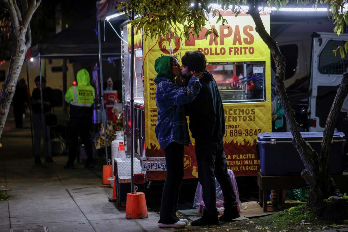 From left, Kalani Robles, 15, kisses Gio Zapien, 16, while waiting for fried chicken and fries at a food stand in Fruitvale. Papas con pollo, a classic Guatemalan food, is readily available in the neighborhood thanks to an influx of Guatemalan immigrants.