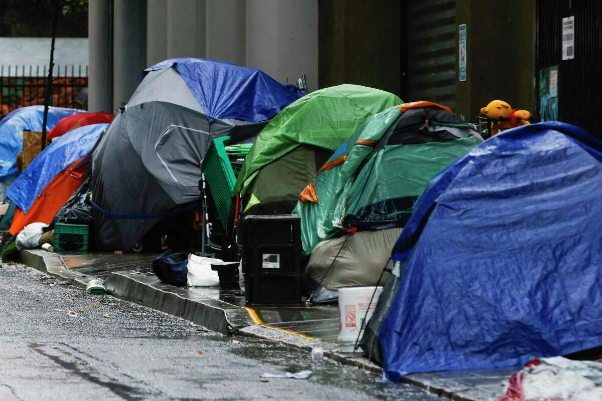 12月，旧金山默特尔街下起大雨，一排帐篷上覆盖着各种防水布和雨伞。