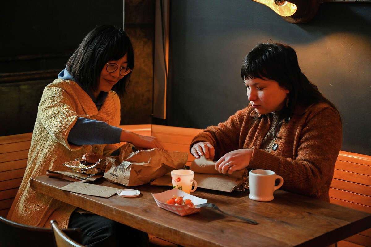 Catherine Pyun and Brianna Meli (left to right) sit inside Ramen Shop's pop-up restaurant Egg Pals in Oakland, Calif., on Sunday Dec. 18, 2022. Both ordered bacon sands, a palate cleanser (plate of fruit) and coffees.