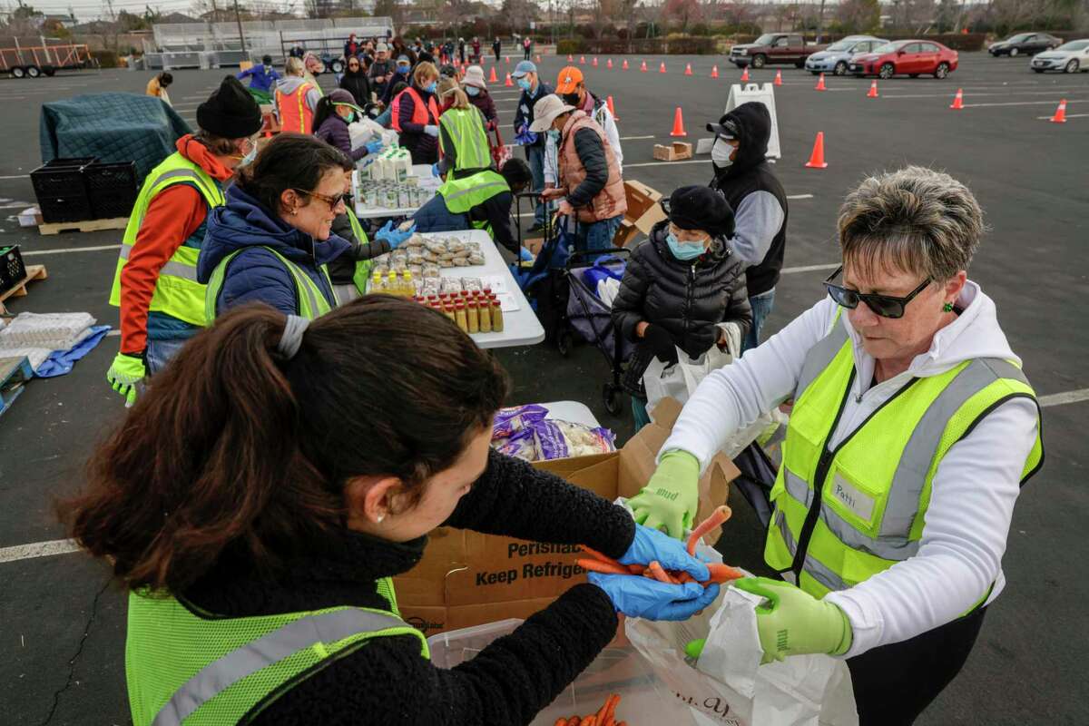 Volunteer Patti Brewer (right) helps people in line for food during the Second Harvest food distribution at the San Mateo Event Center in San Mateo, Calif., on Thursday.