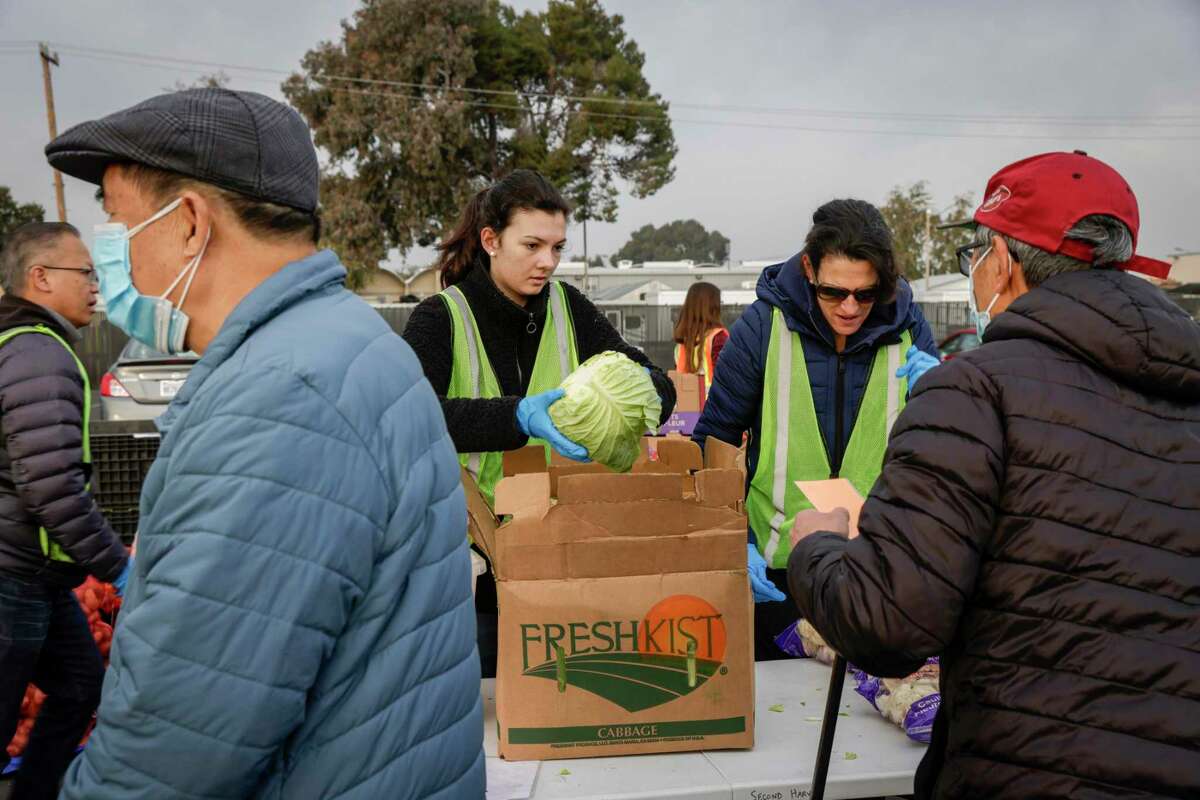From left, volunteers Emilie Kofford, 16, and her mother Nicole hand produce to people standing in line for food during the Second Harvest’s food distribution in San Mateo, Calif., on Thursday.