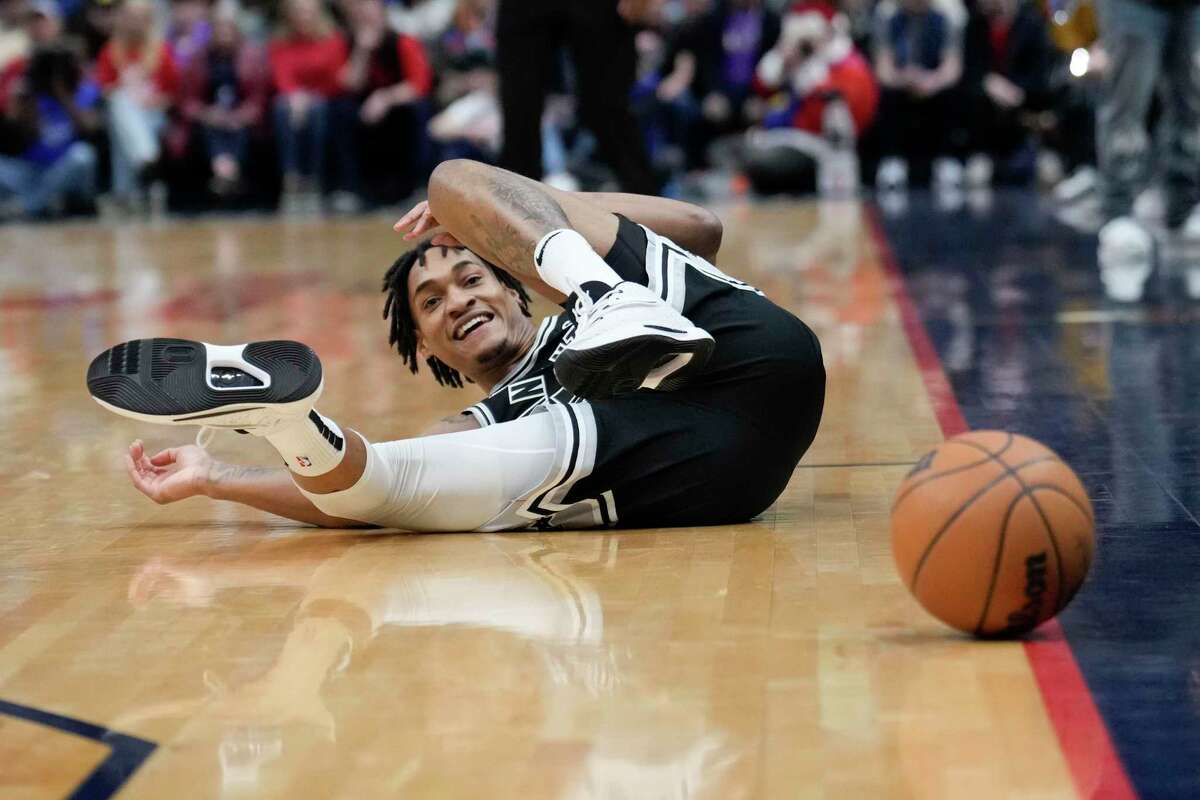 San Antonio Spurs guard Devin Vassell (24) falls to the court as he watches the ball go out of bounds after chasing the ball down in the first half of an NBA basketball game against the New Orleans Pelicans in New Orleans, Thursday, Dec. 22, 2022. (AP Photo/Gerald Herbert)