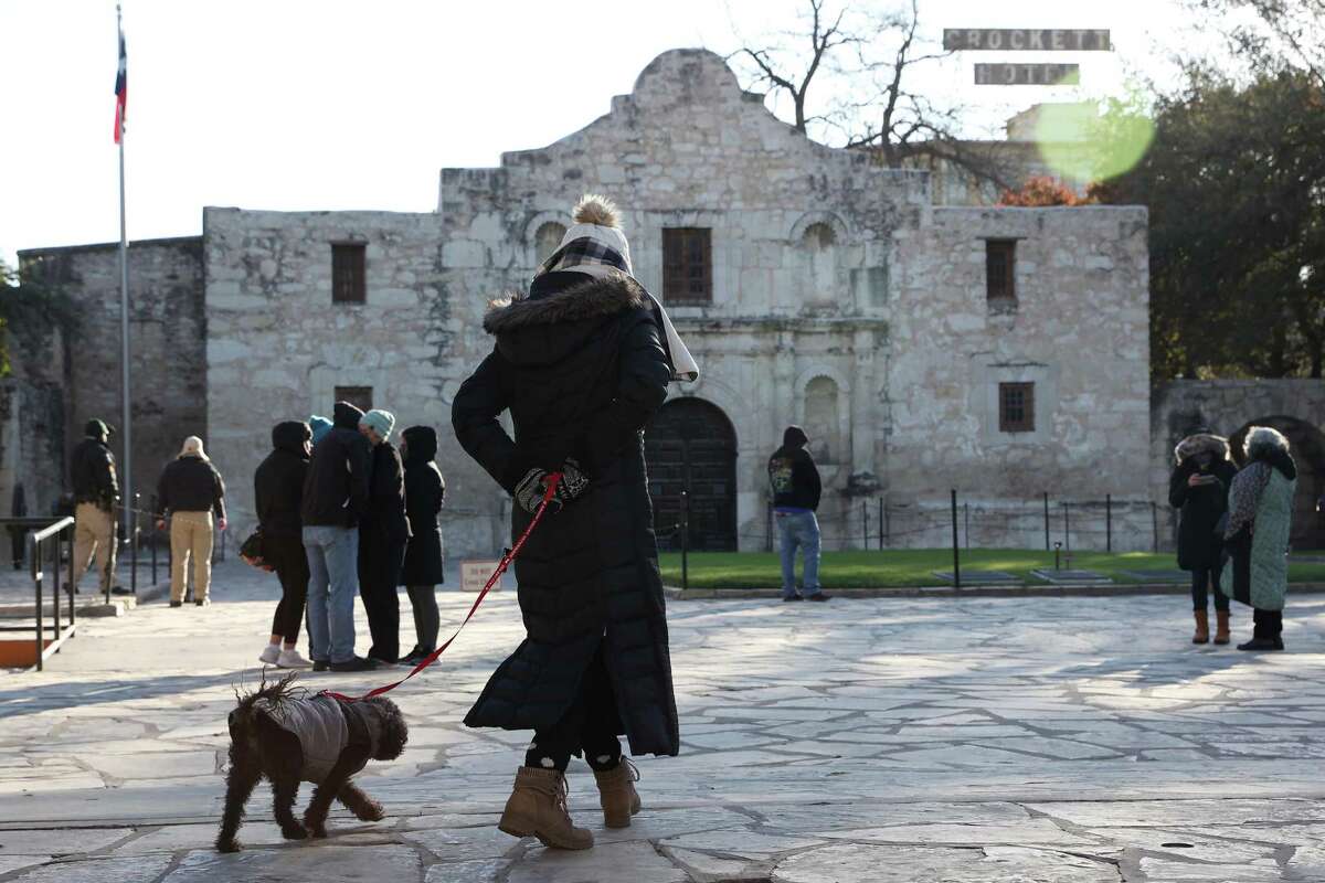 A woman walks her dog in a coat at Alamo Plaza during chilly weather.
