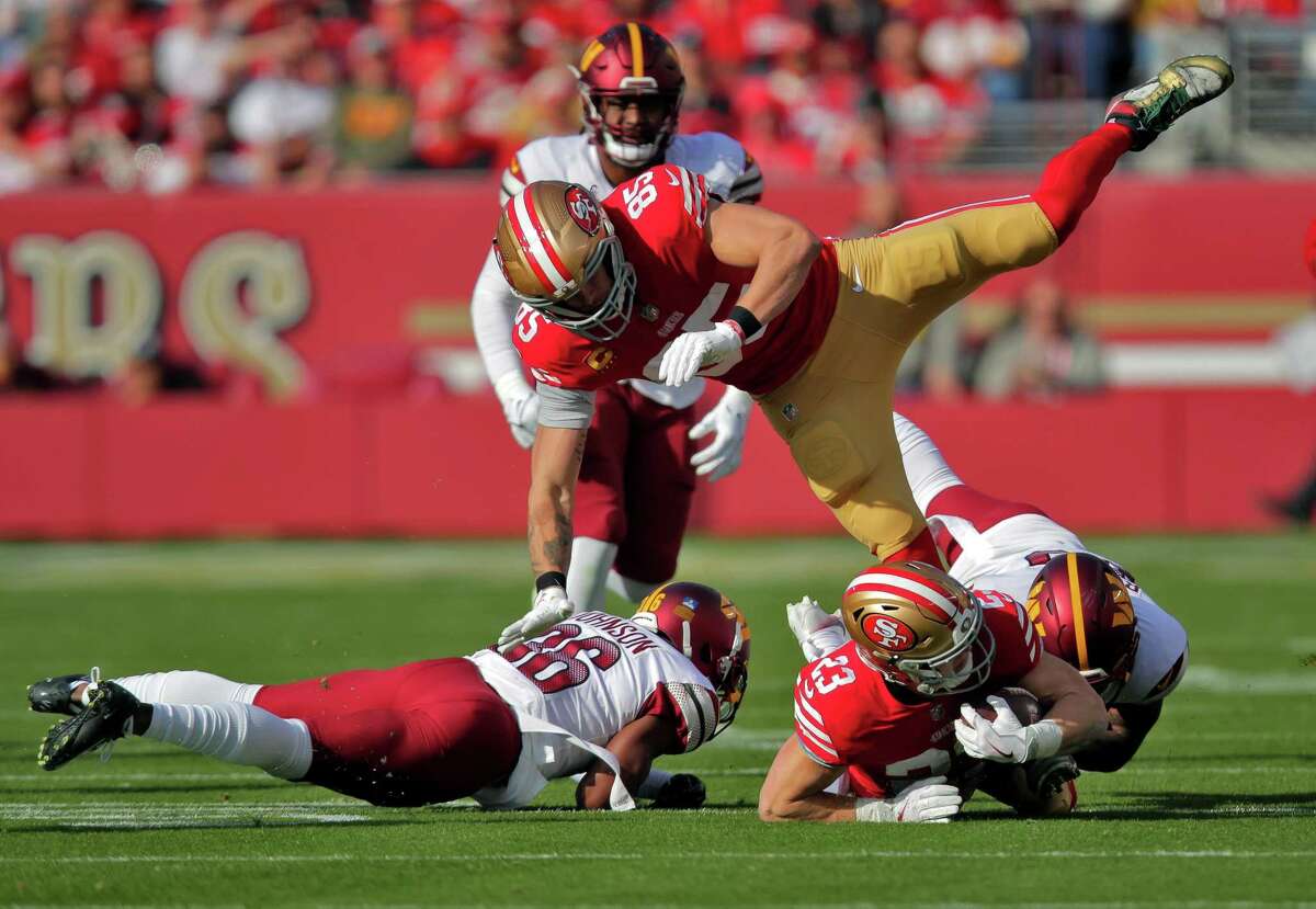 George Kittle (85) leaps over a falling Christian McCaffrey (23) after his run in the first half as the San Francisco 49ers played the Washington Commanders at Levi’s Stadium in Santa Clara, Calif., on Saturday, December 24, 2022.