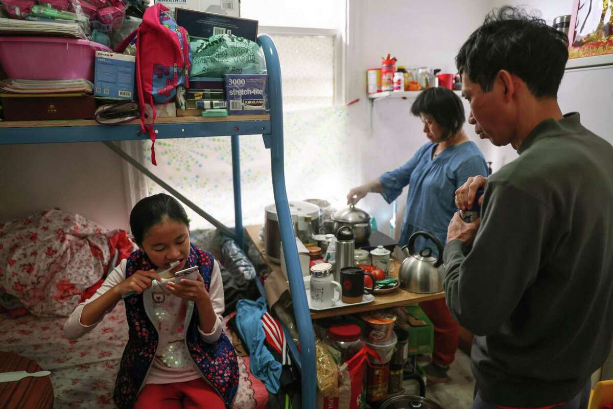 Winnie Tan brushes her teeth while getting ready for school as her parents, Junchang Tan (right) and Qianyan Li, prepare breakfast in their cramped room in Chinatown.