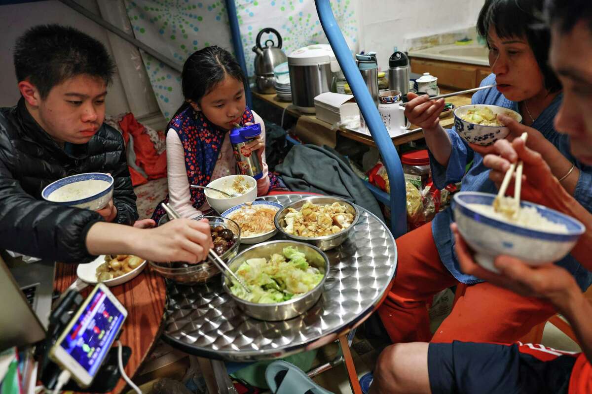 Winnie (center), brother William, and parents Qianyan Li and Junchang Tan eat dinner around a small table in the unit at the Chinatown SRO hotel.