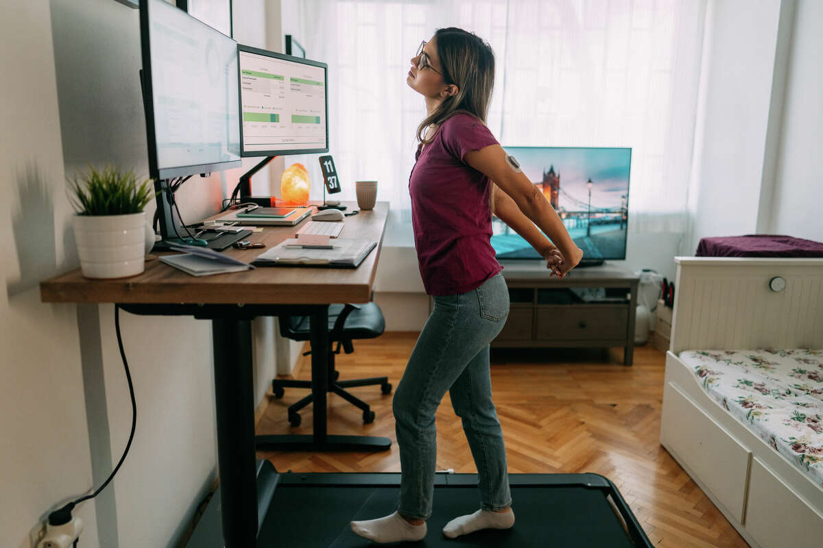 Woman working from home at standing desk is walking on under desk treadmill