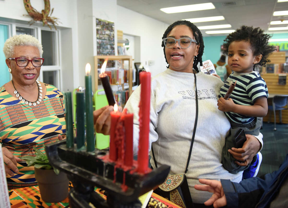 Stamford's Maya Donald, center, and her son, Melson Donald, 2, light a candle beside South End Branch supervisor Josephine Fulcher-Anderson during the Kwanzaa Community Gathering and Celebrations event at Ferguson Library's South End Branch in Stamford, Conn. Thursday, Dec. 29, 2022. Folks celebrated day four of Kwanzaa on Thursday by learning the principle of Ujamaa, meaning cooperative support, through a paper weaving activity. Another event is planned at the South End Branch on Saturday to teach the principle of Kuumba, meaning creativity, with a coloring activity.