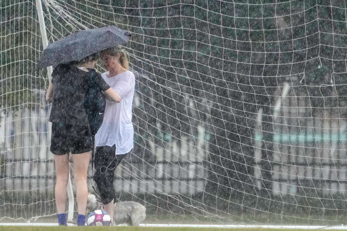 A pair of women huddle under an umbrella on a soccer field during a rain storm at Rice University on Thursday, Dec. 29, 2022 in Houston.