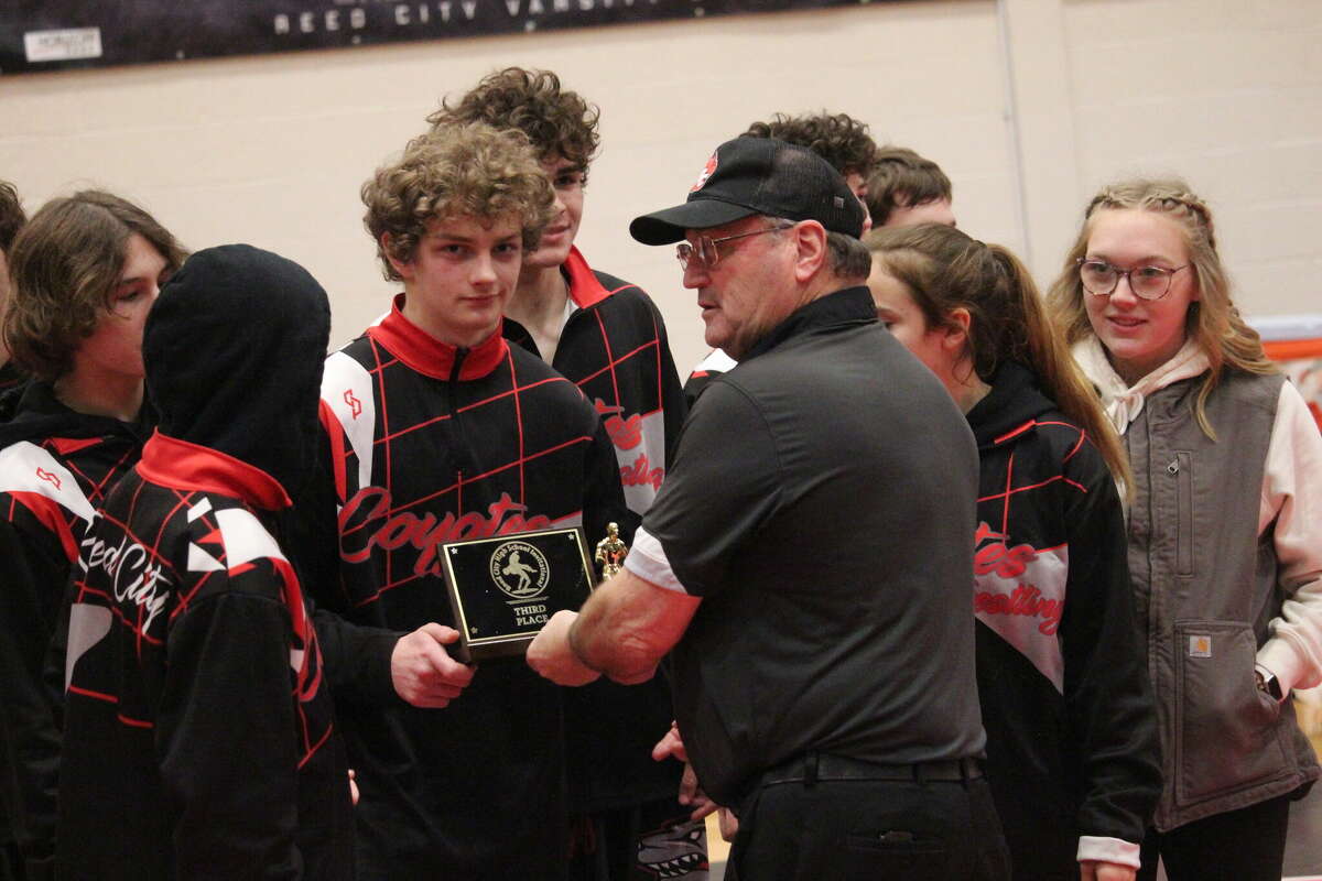 Reed City wrestling coach Roger Steig hands the third-place plaque to his team after Thursday's match.
