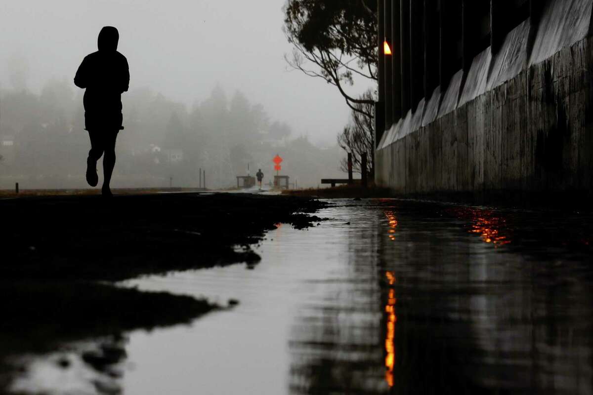 A runner heads down the Mill Valley-Sausalito Path past large puddles during a brief respite from the atmospheric rain.