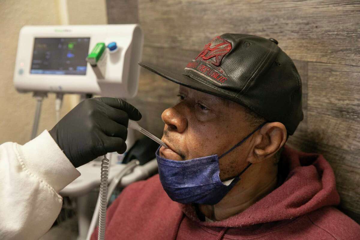 Medical assistant intern Any Meza takes the temperature of patient Ronald at the Roots Community Health Center in Oakland in November. COVID remains a threat statewide heading into the new year.