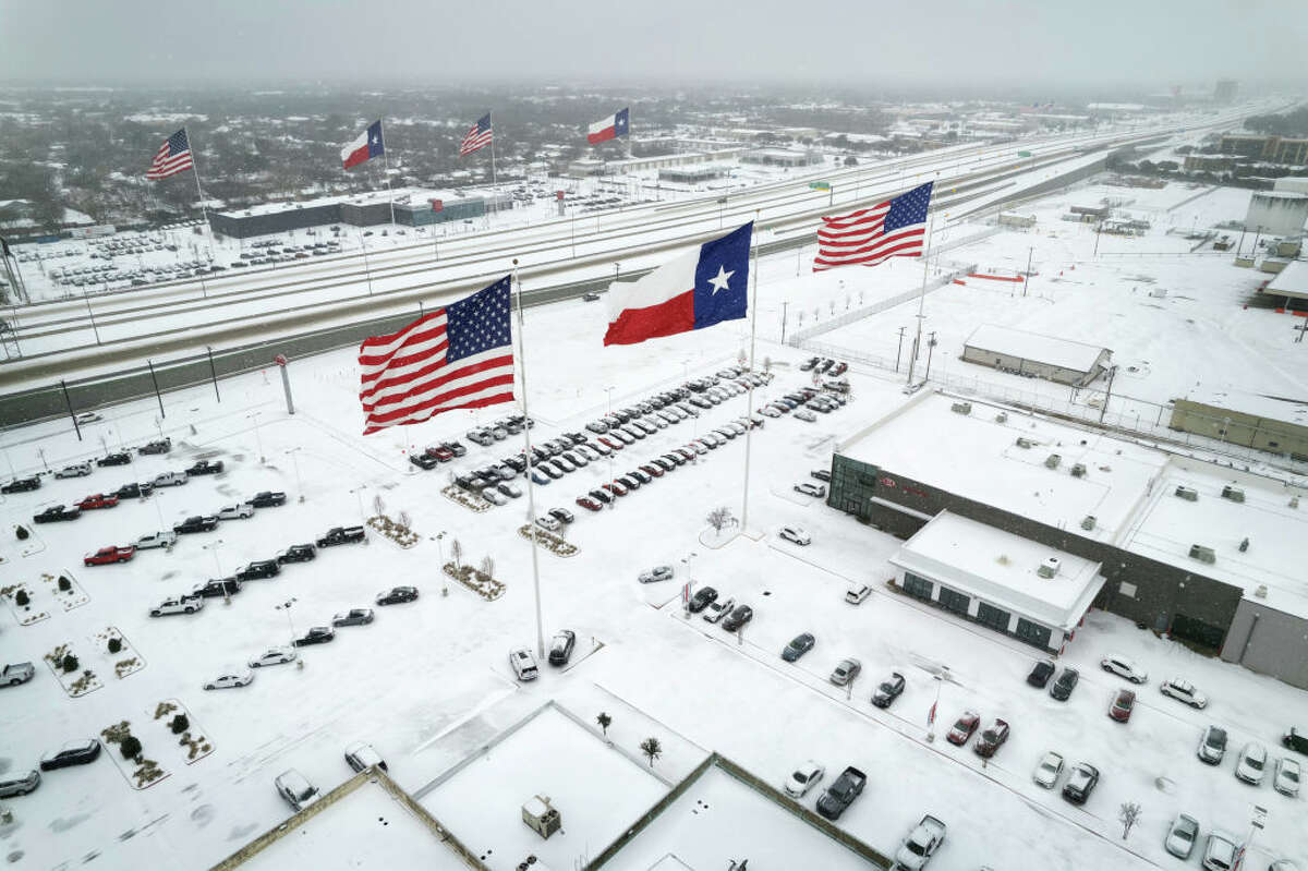 IRVING, TEXAS - FEBRUARY 03: In an aerial view, U.S. and Texas state flags fly over car dealerships as light traffic moves through snow and ice on U.S. Route 183 on February 03, 2022 in Irving, Texas. A winter storm blanketed much of Texas with snow, sleet and freezing rain, as it swept east, also affecting much of the midwest and eastern United States.