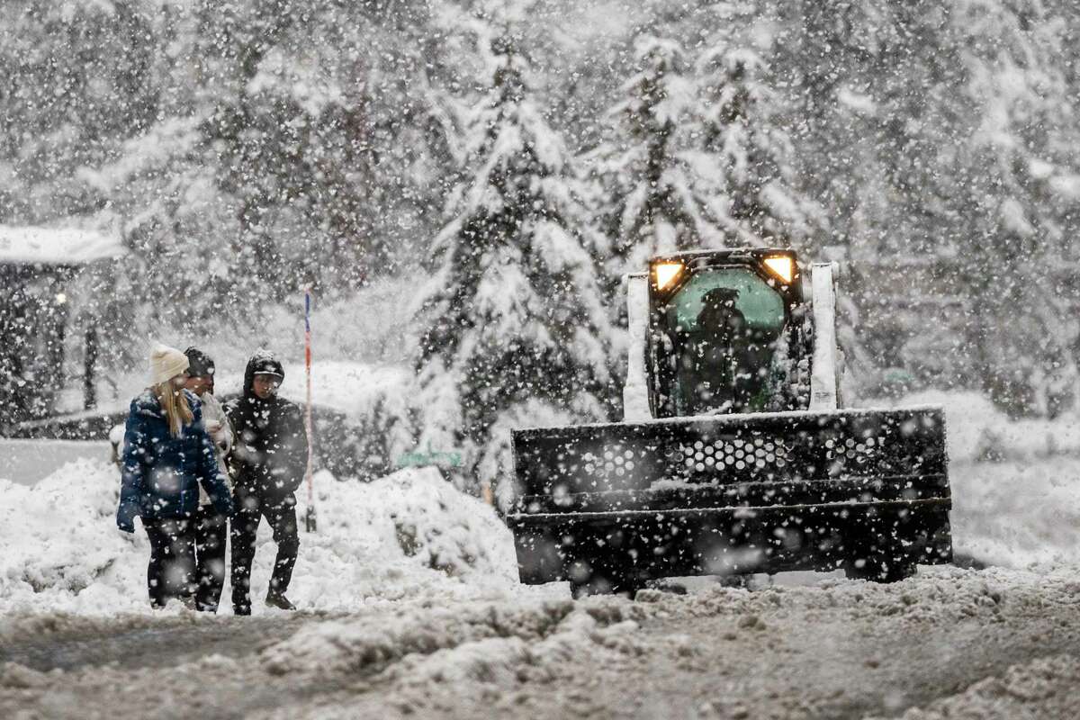 Pedestrians walk along a road as a snow plow works in South Lake Tahoe, Calif., Saturday, Dec. 31, 2022. A winter storm warning has been issued for the greater Lake Tahoe area until Sunday.