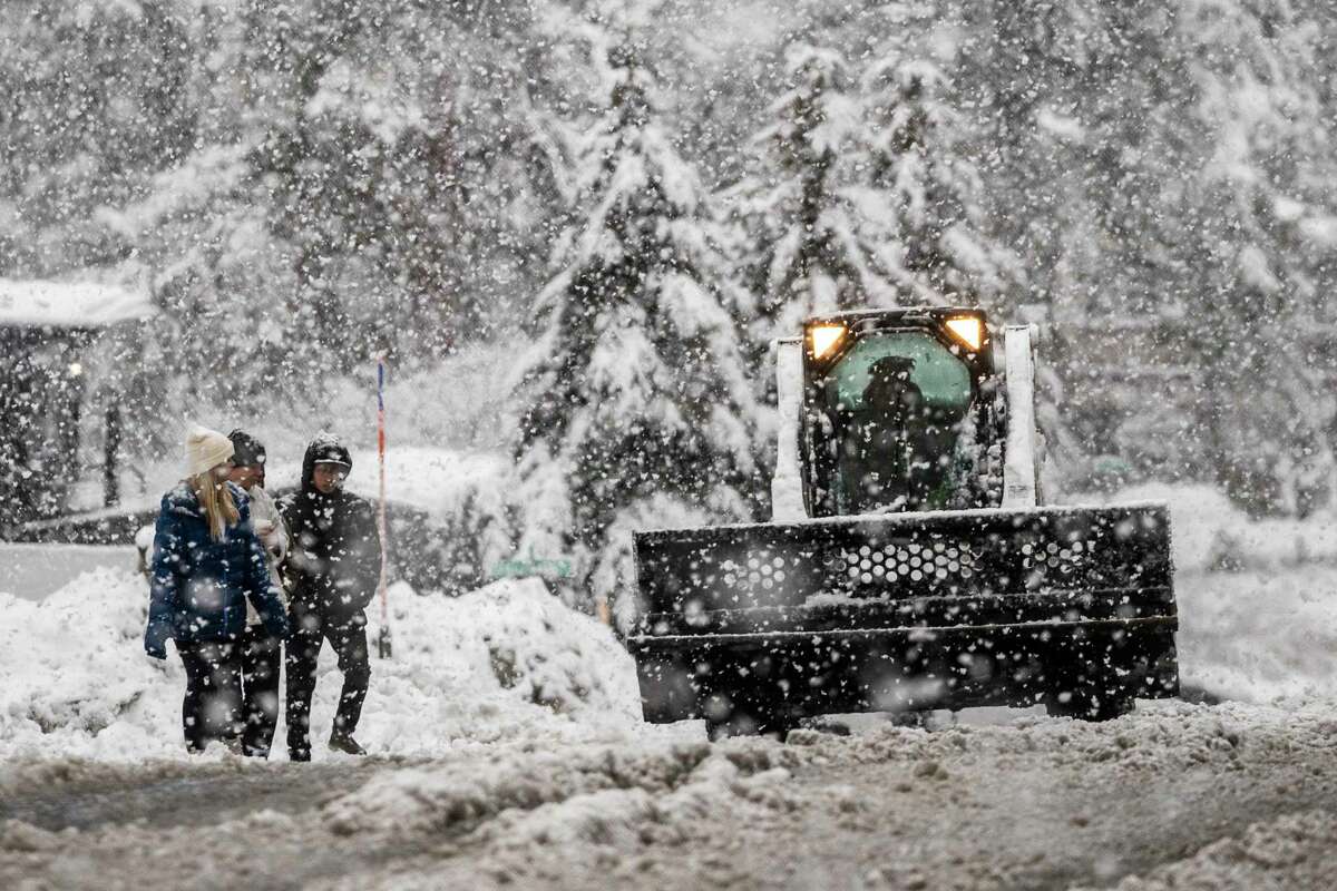 Pedestrians walk along a road as a snow plow works, Saturday, Dec. 31, 2022, in South Lake Tahoe, Calif. A winter storm warning has been issued for the greater Lake Tahoe area through Sunday.