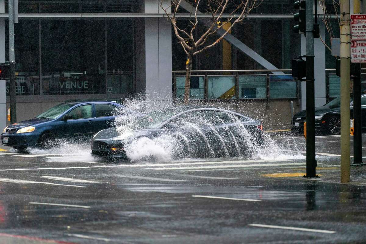 A car   splashes done  a ample  puddle that partially fills the intersection astatine  Howard Street and Fremont Street successful  San Francisco connected  Saturday, Dec. 31, 2022.