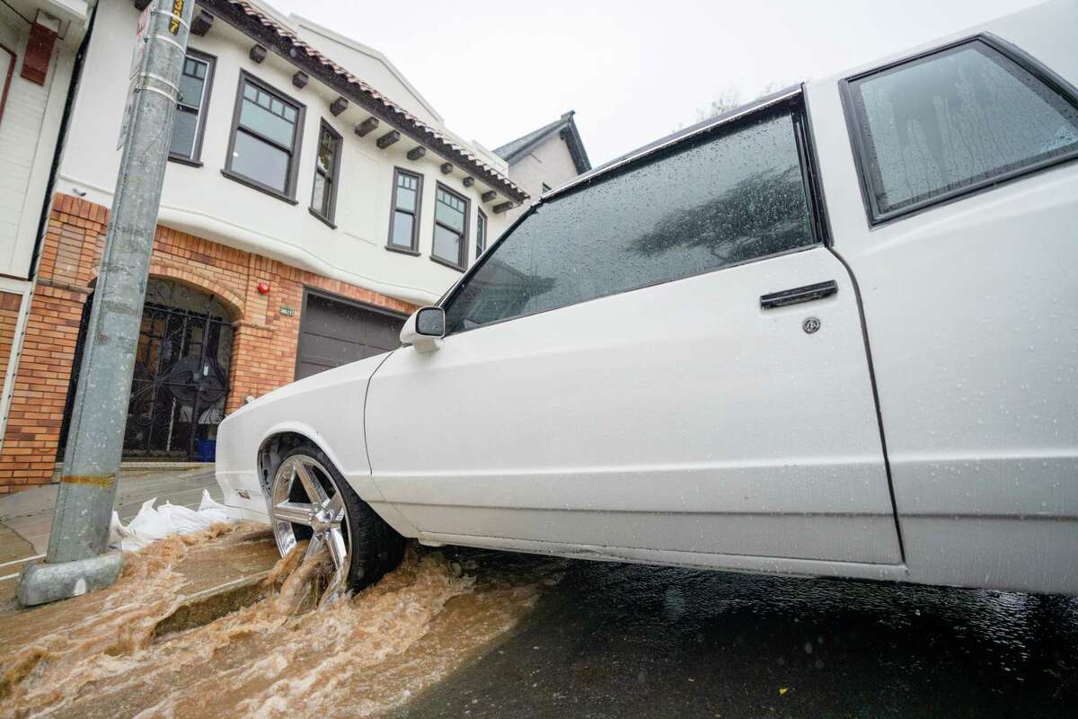 Water flows through a car wheel as muddy water flows down Folsom Street in Bernal Heights, San Francisco, California, Saturday, Dec. 31, 2022.