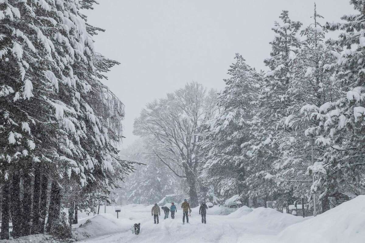 People walk along a snow-covered road in Tahoe Keys community in South Lake Tahoe, Calif. on Saturday, Dec. 31, 2022. A winter storm warning has been issued for the greater Lake Tahoe area until Sunday.