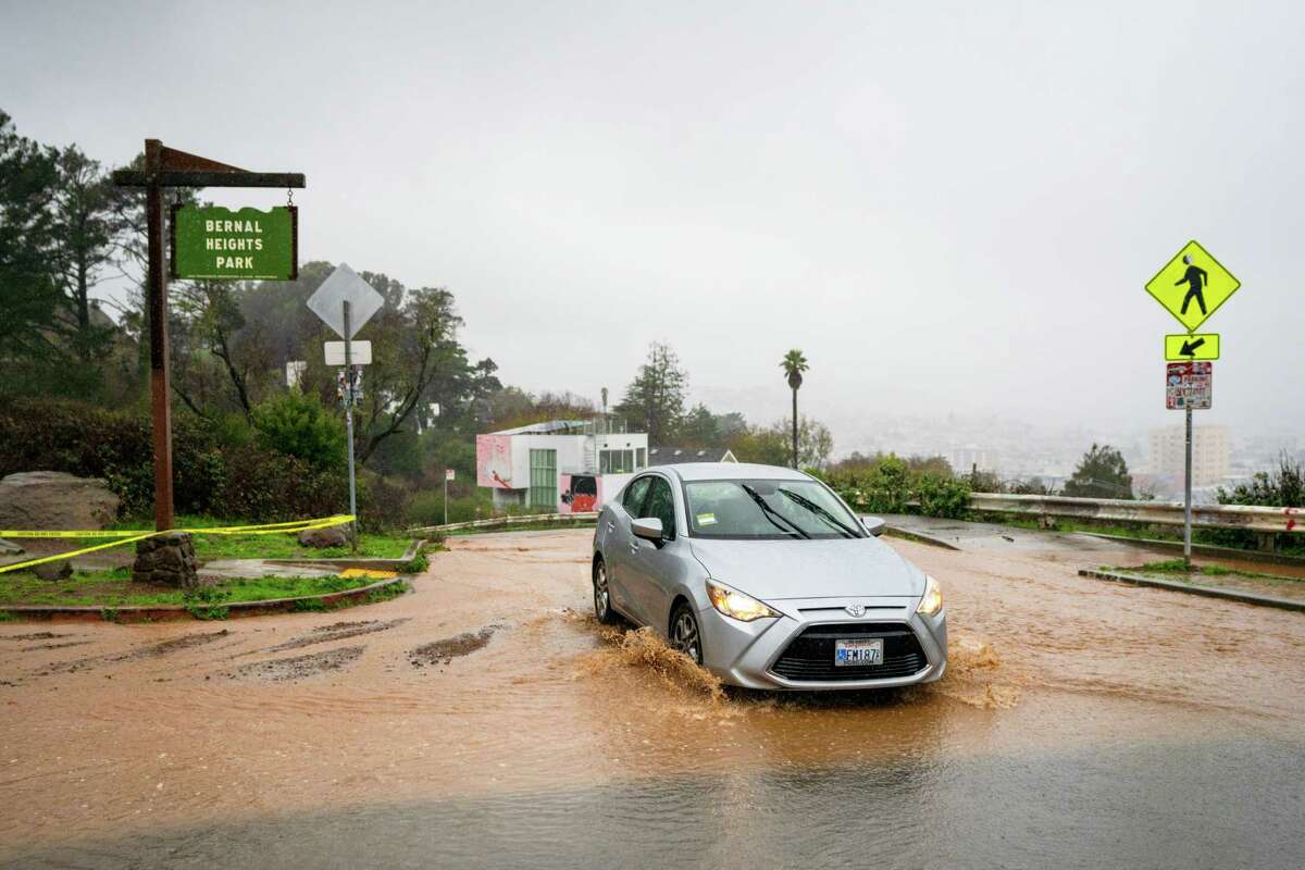A car passes through mud and water as it streams down the road at the Bernal Heights Park along Bernal Heights Boulevard in Bernal Heights in San Francisco, Calif. on Saturday, December 31, 2022.
