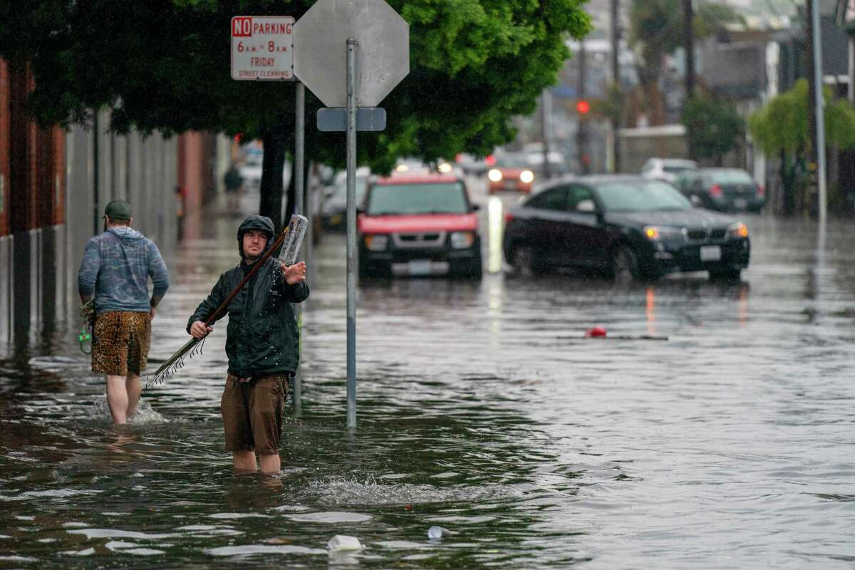 Οι άνθρωποι προσπαθούν να ανοίξουν αποχετεύσεις καταιγίδας για να βοηθήσουν στην ανακούφιση από τις πλημμύρες κατά μήκος της 14ης οδού στην περιοχή Mission του Σαν Φρανσίσκο στις 31 Δεκεμβρίου 2022.