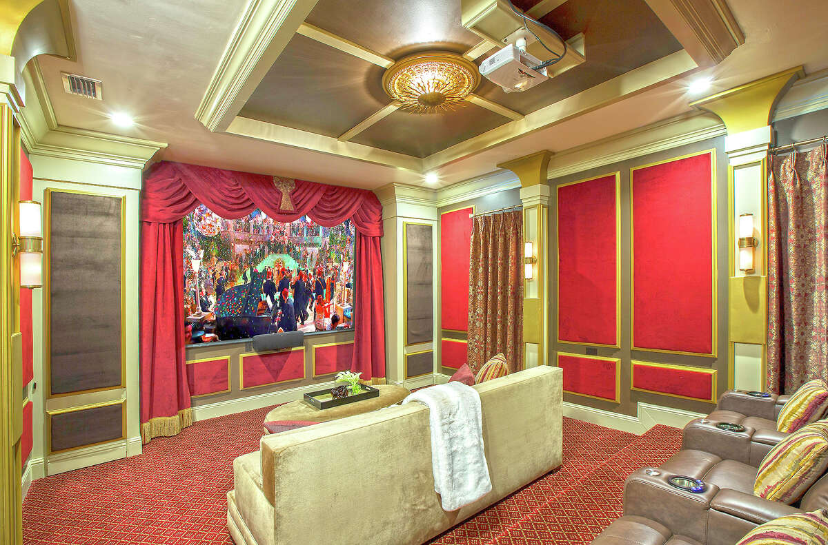 A home theater with red velvet on the wall panels. Champagne-hued velvet is on the big couch in foreground.