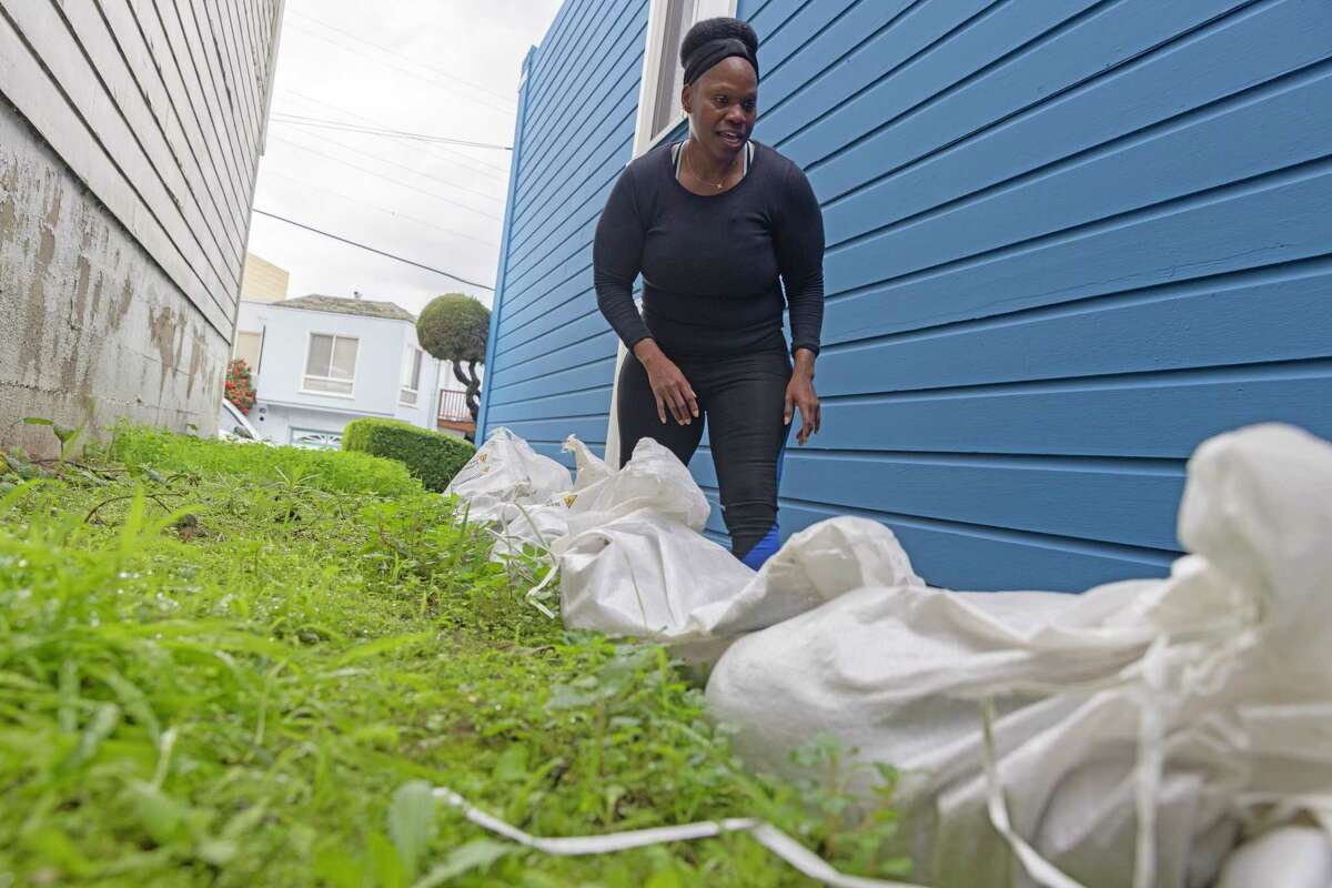 2023年1月3日星期二，加利福尼亚州旧金山，Ifeyinwa Nzerem放下沙袋，试图防止即将到来的风暴造成的洪水。Nzerem的家在Silver Terrace社区的一座山上，她的后院在上周的风暴中被淹没了。Nzerem希望这次用她从城市紧急分配地点捡来的沙袋来防止洪水。
