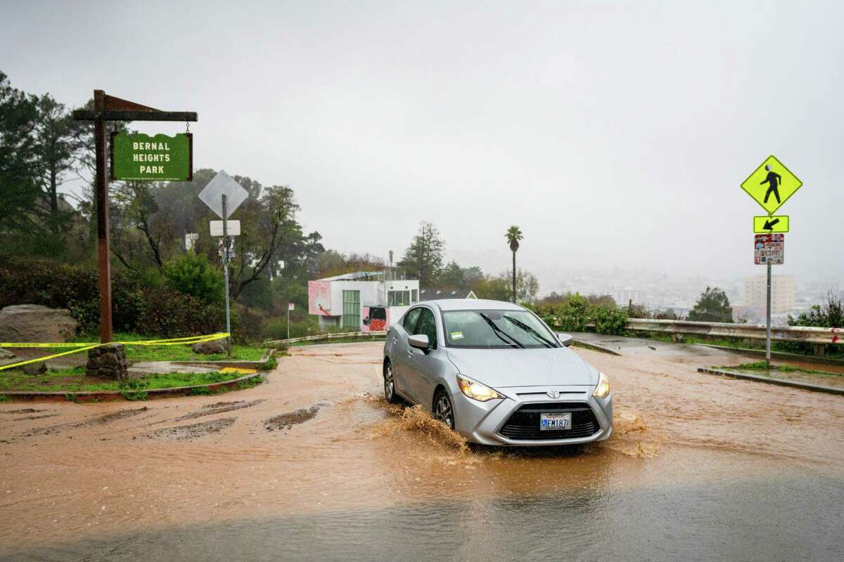 2022年12月31日，周六，一辆汽车在旧金山伯纳尔高地公园的道路上穿过泥泞和水。