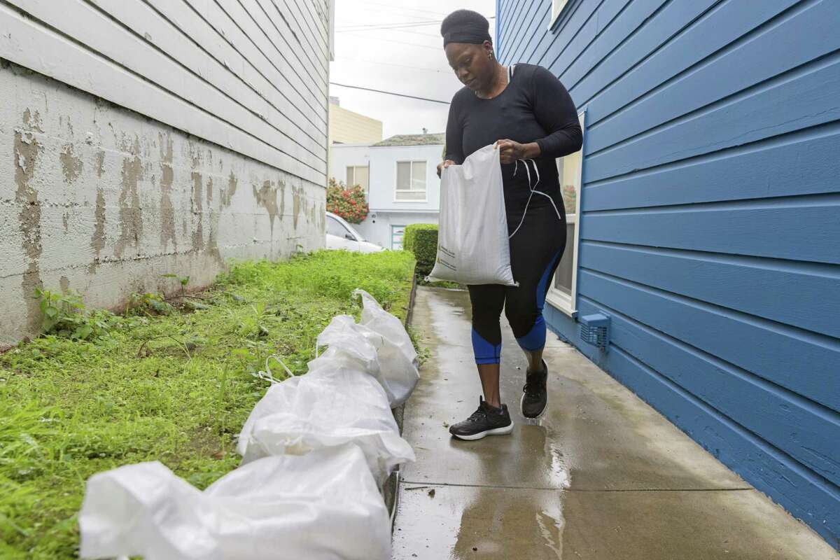2023年1月3日星期二，加利福尼亚州旧金山，Ifeyinwa Nzerem放下沙袋，试图防止即将到来的风暴造成的洪水。Nzerem的家在Silver Terrace社区的一座山上，她的后院在上周的风暴中被淹没了。Nzerem希望这次用她从城市紧急分配地点捡来的沙袋来防止洪水。