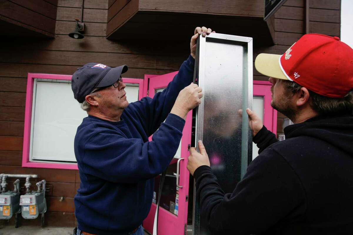 2022年1月3日，Pink Onion的老板Matthew Coric(右)和他的父亲Angelo Coric(左)在教会区餐厅前安装防洪门时，将氯丁橡胶垫圈放在金属片上。