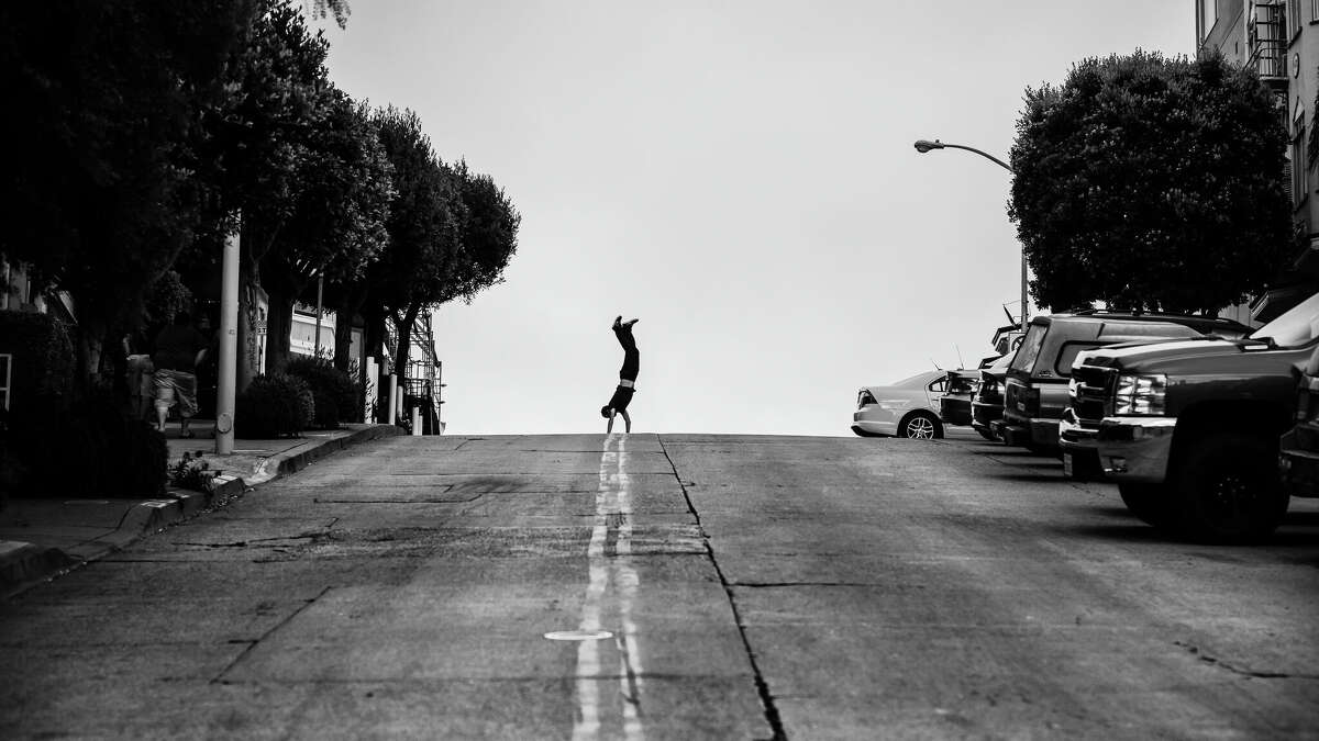 A man does a handstand on a hill in San Francisco.