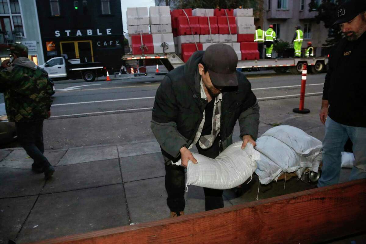 Alejandro Cortez adds sandbags to a makeshift barrier outside Hilde Brando's furniture in the Mission neighborhood on Tuesday.