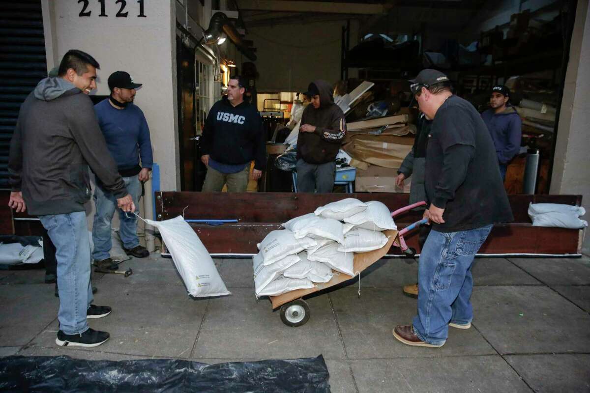 Owner Cleto Gonzalez rolls sandbags to add to a makeshift barrier built with the help of his employees outside Hilde Brand Furniture in the Mission District on Tuesday.