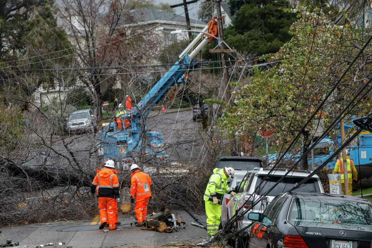PG&E utilities workers clear a fallen tree which took down some power lines next to Bella Vista Elementary School in the Bella Vista neighborhood in Oakland, Calif., on Wednesday, January 4, 2023.
